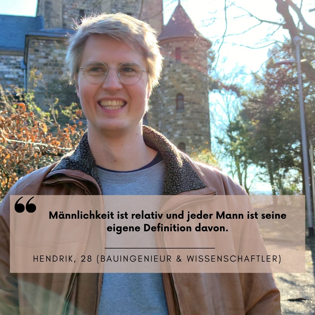 Ein Mann mit brauner Jacke steht vor einem Baum. Im Hintergrund ist eine altes Gemäuer zu sehen. Die Sonne scheint.