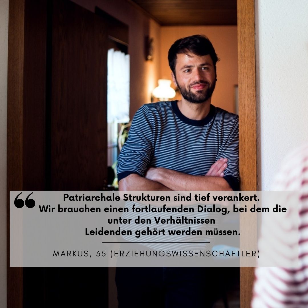 Junger Mann (Markus, 35) lehnt mit verschränkten Armen in einem Türrahmen. Er trägt ein gestreiftes Shirt und steht einer Person gegenüber, die er anlächelt.